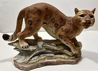 Front view of the porcelain snow leopard figurine on its base, showing the animal's stance and detailed spotted coat.