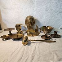 Full view of the brass collection showing all items: King Tut bust, whale and eagle figurines, gavel, various candle holders, and small bowls arranged on fabric background.