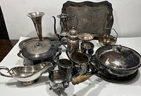 Full lot view showing all silver plated items on table including trays, teapots, cups, gravy boat, flower vase, and lidded bowl