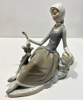 Front angled view of porcelain shepherdess girl figurine sitting with dove on hand.