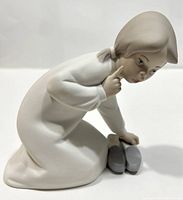 Front side view of matte finish Lladró porcelain figurine showing kneeling girl and adult shoes in front of her.