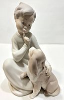 Front angled view of the porcelain figurine showing child and puppy with finger to lips.