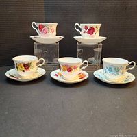 Five Queen Anne fine bone china teacups and saucers, each with floral patterns and gold trim, arranged on stands and on tabletop.