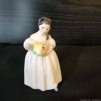 Side view of the Royal Doulton Mandy figurine showing the girl holding a yellow bonnet with floral details.