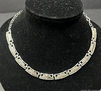 Front view of the silver tone choker necklace displayed on a black velvet stand showing rectangular linked segments.