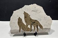 Full view of the soapstone wall plaque showing two howling wolves and the moon with black stand support.