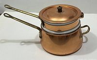 Side view of vintage copper double boiler showing the long wrought iron handles and copper lid with black knob.