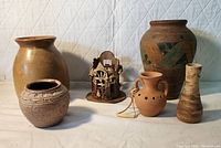 Wide view showing all six pottery and wooden items arranged on a white quilted background under white light.