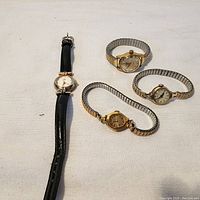 Four vintage ladies watches with varying band types photographed on a light surface.