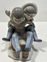 Front view of porcelain figurine of two Eskimo children riding a wooden sleigh, showing detailed clothing and facial expressions.