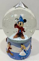 Front view of snow globe showing Mickey Mouse with blue wizard hat and red robe inside the globe, with detailed base characters including Alice and a dwarf.