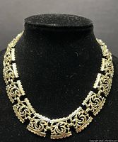 Full view of gold tone ornate link chain choker necklace on black display stand showing overall design and length.