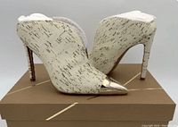 Back view of both shoes showing white cork texture and metallic pointed toe caps, placed on a brown box.