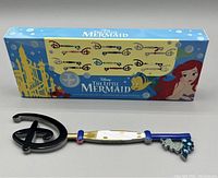 Two images showing the front side of the mystery keys and their themed box featuring The Little Mermaid artwork and character details.