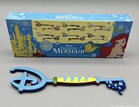 Two collectible Disney The Little Mermaid keys themed after characters Flounder and Sebastian, each shown together with the original series box.