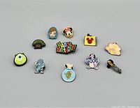 Lot of 11 Disney-themed colored enamel pins laid flat on a plain gray surface.