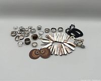 Photo showing various rings, shell pieces, wooden-look earrings, black pendants, and metal jewelry parts spread out on a white surface.