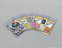 Seven trading cards displayed in clear plastic sleeves, six of which are Pokémon cards.