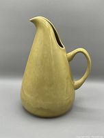Side view of tall ceramic pitcher in mustard yellow with curved spout and handle, smooth glaze surface.