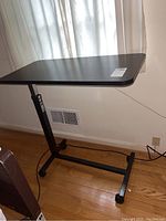 Full view of bedside tray table showing black rectangular flat tabletop and adjustable metal stand.