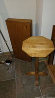 Photo shows a vintage wooden cabinet standing vertically against the wall next to a Hagerty Cohasset wooden octagonal side table with a tripod base.
