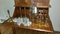 Overview of all items including brass candlesticks, glass votive holders with white candles, and the tall glass hurricane shade on a wooden surface.