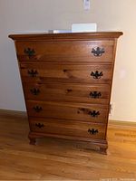 Front view of wooden chest of drawers showing five drawers with metal handles, some scratches visible on drawer fronts.