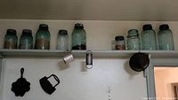 Shelf with six Mason jars with contents, metal measuring cup and metal funnel hanging below shelf.