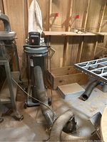 Full view of Delta dust collector system on wheeled cart with hoses attached, placed in basement workshop area with wood walls.