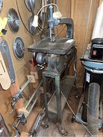 Full view of Delta jig saw on metal stand among other blades and tools in basement workspace.