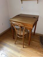 Desk and chair set showing the desk with hinged top and cane seat chair positioned in a corner on wooden floor