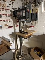 Front view of the Craftsman drill press mounted on a wooden table, showing the base, column, and workspace area with a drill chuck and a drill bit attached.