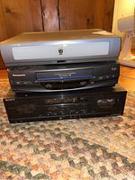 Full view of TiVo Series 2 DVR on top, Panasonic VHS VCR in middle, and Sony TC-WR570 cassette deck at bottom on carpeted floor.