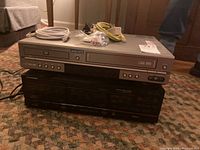 Two stacked electronics devices, Samsung DVD-VCR combo on top, Pioneer tape deck below, with cables on top.