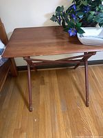 Wooden folding table showing full tabletop and leg structure against a wall with decoration on top.