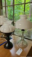 Two hurricane lamps displayed on a wooden surface by a window, showing the overall shapes, bases, and shades.