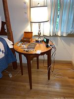 Side view of the wooden handmade side table with circular top and tapered legs, showing water damage, with touch lamp placed on top along with some small items.