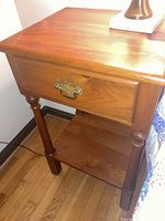Wooden nightstand with single drawer and lower shelf, showing front and side views, visible scratches on wood finish.