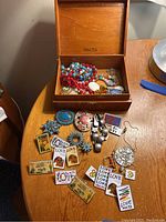 Wooden jewelry box with beaded necklaces inside and assorted costume jewelry laid out on table including pins and earrings