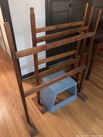 Three vintage wooden quilt racks with horizontal rails and a blue painted wooden step stool in front.
