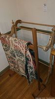 Photo of one wooden quilt rack with antique throw blanket draped over one rail, showing full height and side detail.