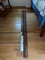 Two rolled fruitwood shades on a hardwood floor next to a bed and chair, one wrapped in plastic packaging, the other unwrapped.