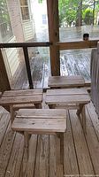 Four matching wooden side tables arranged on a wooden porch floor, showing the tops and legs.