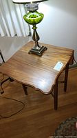Vintage wooden dropleaf table with lamp on top, showing the scalloped edges and wood grain.