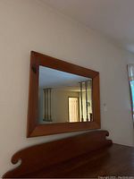 Full view of rectangular wall mirror with wood frame hung on wall above wooden shelf showing size and environment.