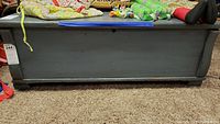 Front view of dark painted wooden blanket chest showing rectangular shape and low feet with visible paint chipping and scratches.
