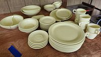 Overall view of the dish set displaying covered butter dish, divided bowl, several plates, bowls, and cups on a wooden table.