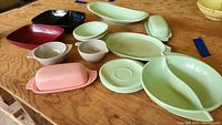 Top view of assorted Boonton Ware melamine dishes on wooden surface showing pastel green and pink covered butter dishes, divided bowl, platters, and serving bowls.