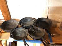 Five cast iron skillets shown together on a wooden surface, showing various sizes and wear.