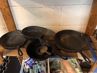 Five cast iron skillets arranged on a wooden shelf, showing various sizes and some rust.